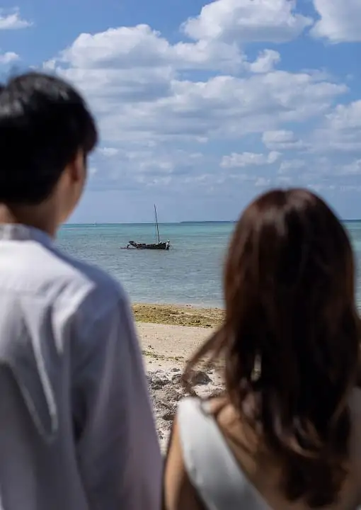 浜辺からサバニを眺める二人